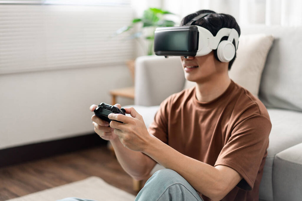 Technology Concept Un hombre que se pone un auricular de realidad virtual y presiona un juego de consola negro mientras está sentado en el suelo. - Foto, imagen