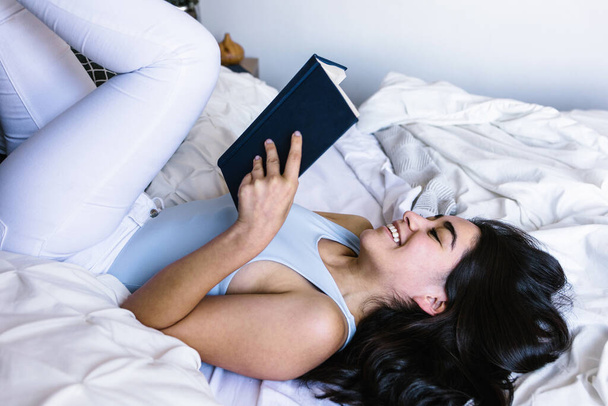 Joven latina leyendo libro y estudiando en la cama en casa en México América Latina - Foto, Imagen