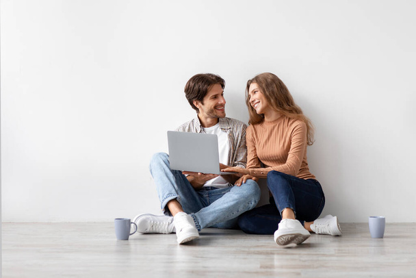 Smiling millennial european man and woman sitting on floor resting from moving at new house, planning interior - Photo, Image