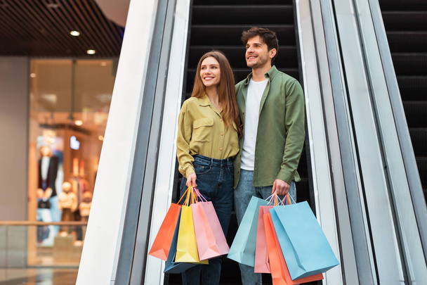 Couple Holding Bags Standing On Moving Stairs Shopping In Mall - Photo, Image