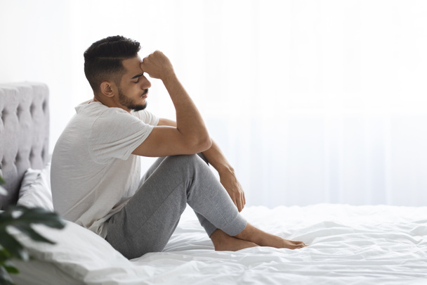 Portrait Of Depressed Young Middle Eastern Man Sitting On Bed In Bedroom - Photo, Image