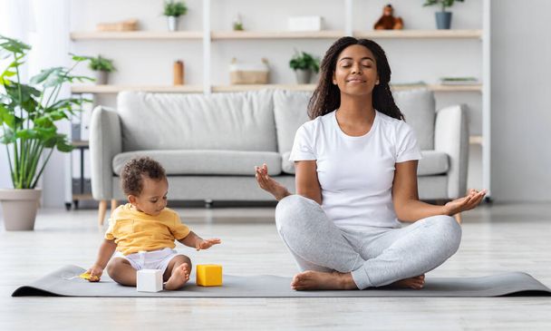 Koncepcja zdrowia psychicznego. Spokojny Szczęśliwy Czarny Matka Medytuje Z Dzieckiem W Domu - Zdjęcie, obraz