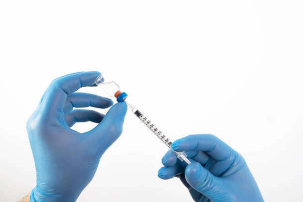 COVID-19 coronavirus vaccine. Vaccination concept. Doctor's hand in blue gloves hold medicine vaccine vial bottle and syringe. - Valokuva, kuva