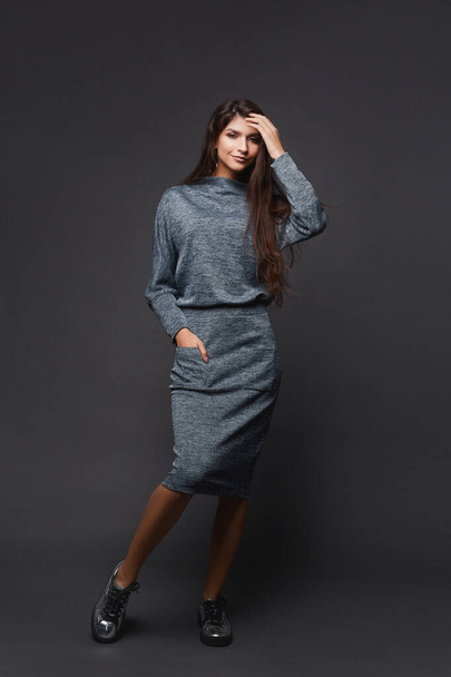 Young pretty woman in knitted dress posing over dark grey background - Photo, Image