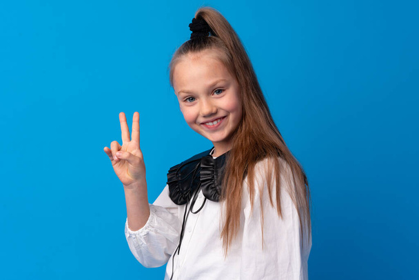 Young teen girl showing a peace symbol with fingers against blue background - Foto, Bild