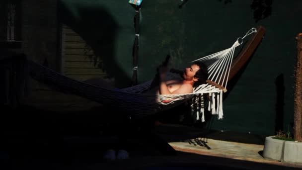 Jeune homme caucasien est bronzer couché sur l'hamac et en utilisant smartphone dans ses mains - Séquence, vidéo