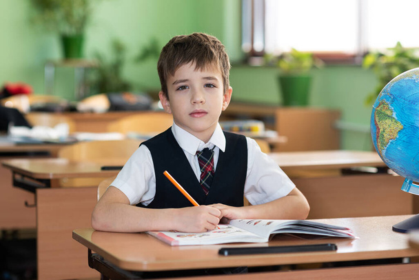 Ein Schuljunge sitzt an einem Schreibtisch mit Schulbüchern und lächelt. Schulleben - Foto, Bild