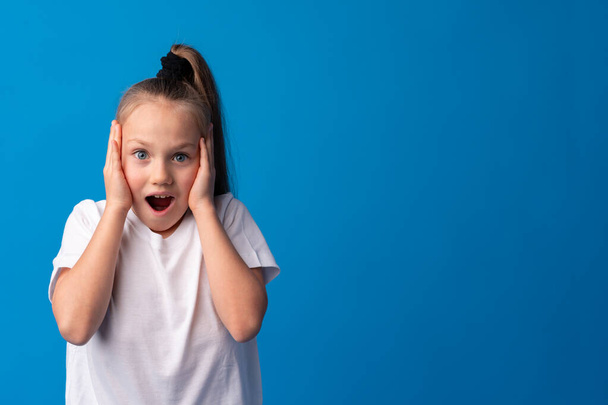 Shocked little girl looking with amazement on blue background - Фото, изображение