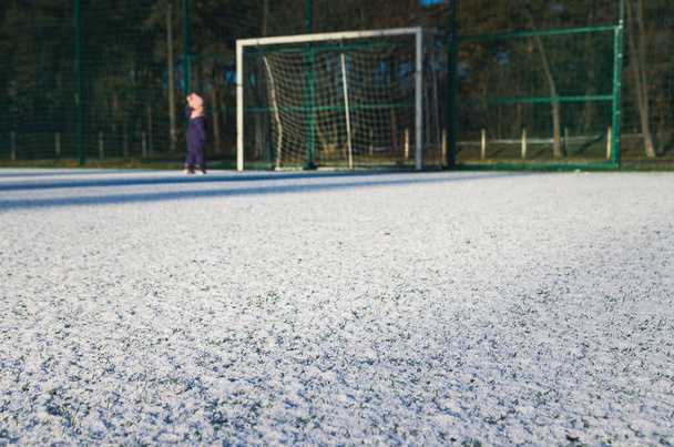 Футбольное поле с искусственной зеленой травой покрыто легким слоем снега. Зеленая трава на футбольном поле видна из-под снега. Любительское футбольное поле. - Фото, изображение