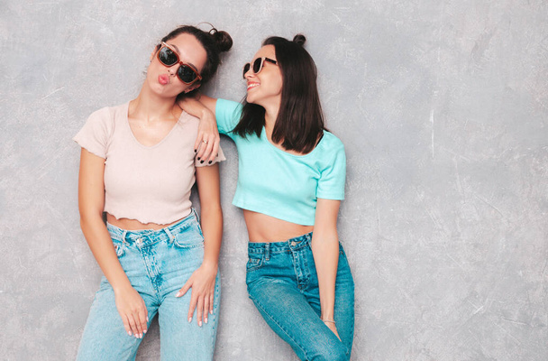 Two young beautiful smiling blond hipster female in trendy summer clothes. Sexy carefree women posing near grey wall in studio. Positive models having fun. Cheerful and happy. In sunglasses - Φωτογραφία, εικόνα