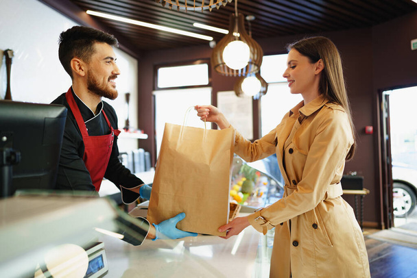 Shop assistant handling shopping bag to female customer in grocery store - Fotografie, Obrázek
