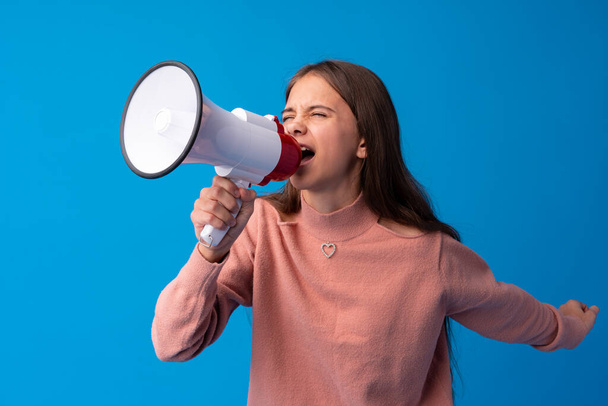 Teen girl making announcement with megaphone at blue studio - Photo, image
