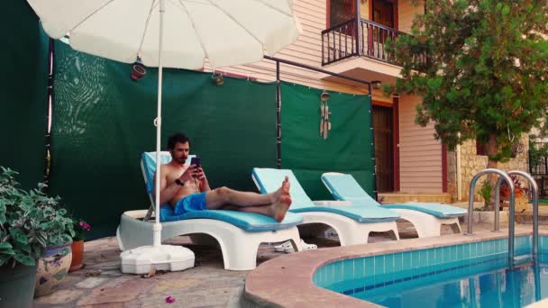Junger Mann in einem Hotel am Pool legt sich auf einen Liegestuhl und beginnt zu reden - Filmmaterial, Video