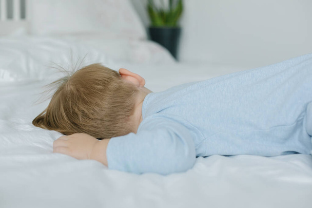 Lindo niño en traje de dormir azul durmiendo en la cama en casa - Foto, imagen
