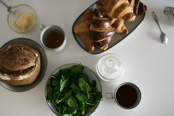 Tasty and healthy breakfast on white table. Croissans, milk, honey, bread. European lifestyle. Mediterranean food. Stylish dishes. Modern interior. Fresh bakery. Spinach. Tea and coffee. Fresh juice - Photo, Image