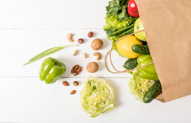 Top view of a paper kraft bag with healthy natural food on a white wooden table. the concept delivery or purchase in the supermarket - Foto, afbeelding