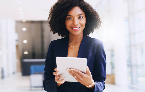 Updating my work schedule. Cropped portrait of an attractive young businesswoman standing alone and using a tablet while in the office during the day. - 写真・画像
