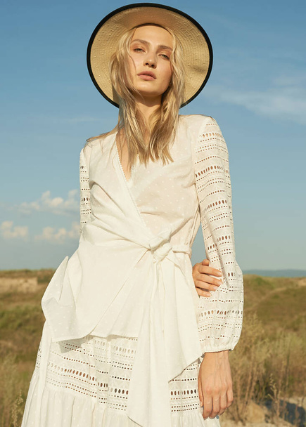 Gorgeous young woman in white romantic clothes on summer field background. Yellow grass, blue sky. Sunny day. Blonde model with big beautiful eyes and nice lips. Calm and balance. Fashionable look   - Φωτογραφία, εικόνα