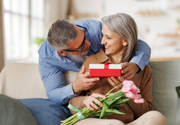 Любящий муж дарит цветы и подарочную коробку на день святого Валентина счастливой удивленной жене - Фото, изображение