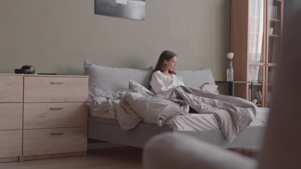 Slowmo πλάνο της νεαρής καυκάσιας γυναίκας με φορητό υπολογιστή που παίρνει πρωινό στο κρεβάτι στο άνετο σπίτι - Πλάνα, βίντεο