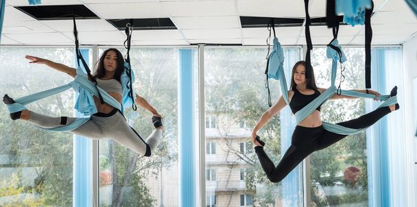 due belle donne in tuta sportiva per l'allenamento mostrano diversi trucchi in amache sportive per lo yoga a mosca. Concetto di volare yoga - Foto, immagini