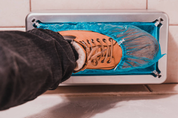 Schuhbezüge und ein Clinthoper, ein Organisator für Einweg-Schuhbezüge im Krankenhaus, ein Mann zieht Stiefelbezüge für Sauberkeit im Zimmer an, eine Maschine für die Montage von Stiefelbezügen. - Foto, Bild