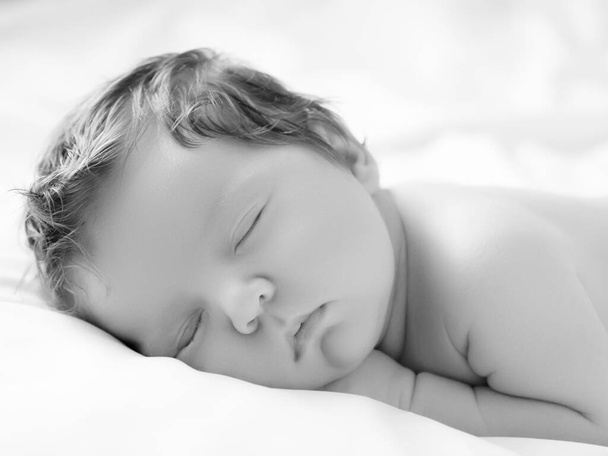Uma menina com rosto sorridente durante o sono. Pequena menina dormindo em cobertor branco. Belo retrato de menina de 14 dias, duas semanas de idade. Maternidade - Foto, Imagem