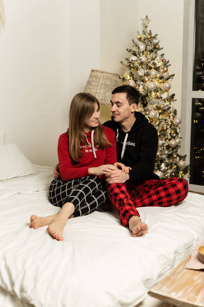 a guy with a girl in pajamas hugging on the bed in the evening. christmas evening. - Fotoğraf, Görsel