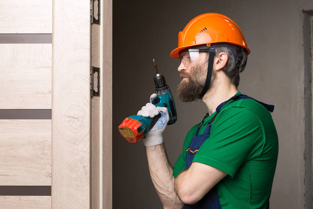 A male locksmith installs a door in an apartment. The guy works with a screwdriver. - Photo, Image