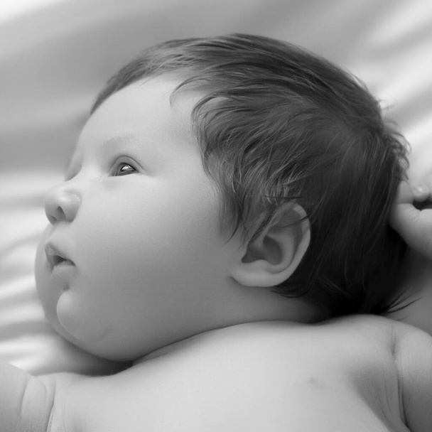 Bonito retrato de primer plano del bebé recién nacido. Acostado en una cama blanca. Lindo recién nacido de 1 mes de edad en sábana blanca en pañal. Cuidado del recién nacido, cólicos, dientes, día del recién nacido - Foto, Imagen