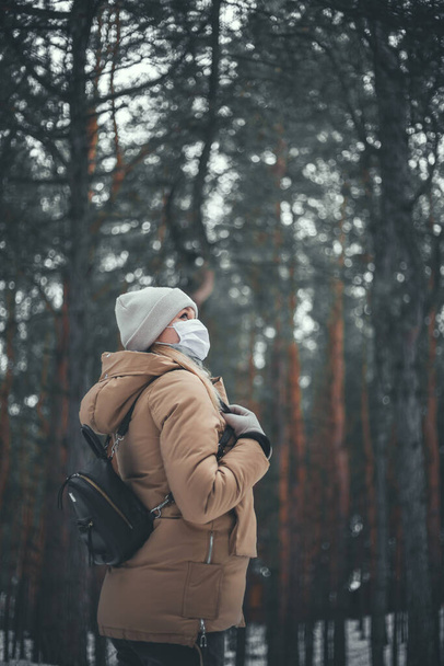 A young girl with blond hair in a medical mask is walking in the forest. - Foto, imagen