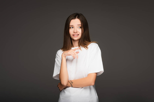 frightened woman in white t-shirt pointing with finger isolated on dark grey - Foto, immagini