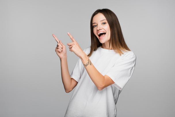 thrilled woman pointing with fingers while looking at camera isolated on grey - Foto, immagini