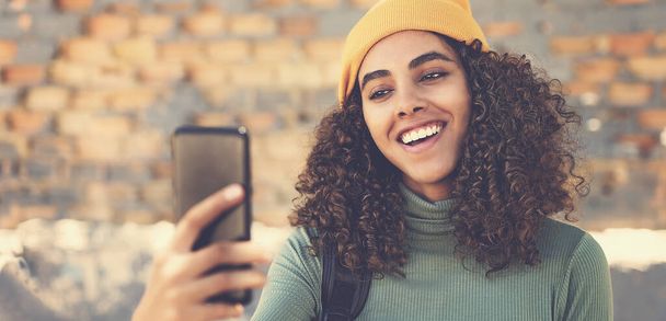 Video call of laughing latin american female young adult with knit hat outdoor in urban city style - 写真・画像