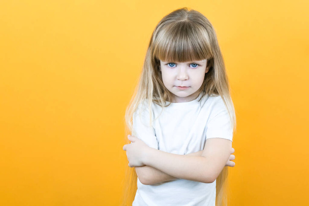 Naughty child. Disobedience problem. discipline punishment. Portrait of cute angry offended little girl in white with crossed arms isolated on yellow copy space background. - Photo, Image