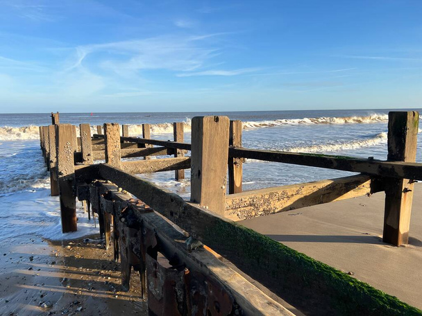 Paysage de barrière côtière sur la plage de sable fin pour protéger de l'érosion avec plate-forme en bois dans l'eau de mer par temps frais et lumineux avec ciel bleu et vagues basses en hiver à Gorleston Norfolk East Anglia uk - Photo, image
