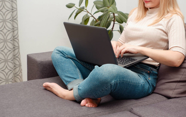Styl życia wolnego strzelca. Radosna kobieta pracująca na laptopie i przeglądająca online na kanapie w domu. Skupienie selektywne - Zdjęcie, obraz