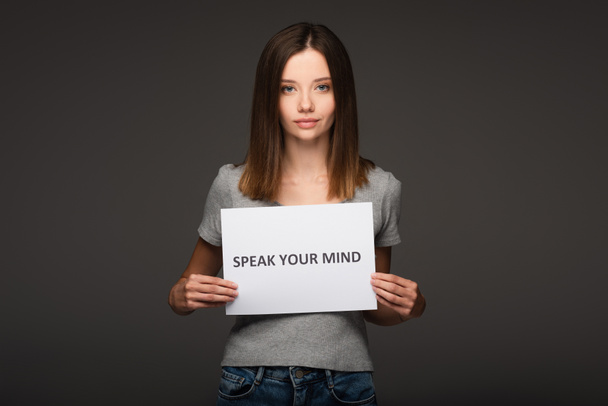 young woman holding card with speak your mind phrase isolated on grey - Photo, Image