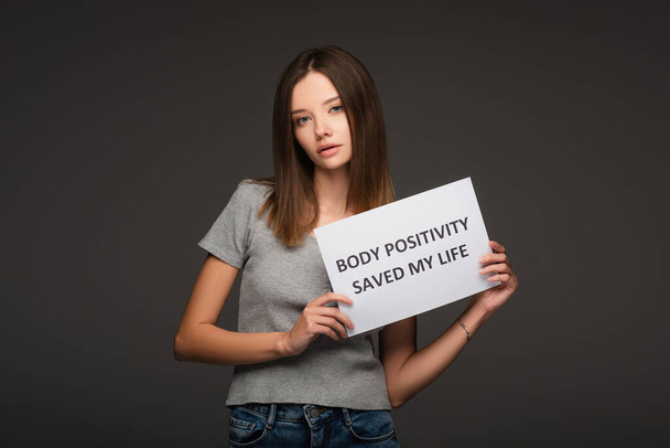 brunette woman holding paper with body positivity saved my life lettering isolated on grey - Photo, Image