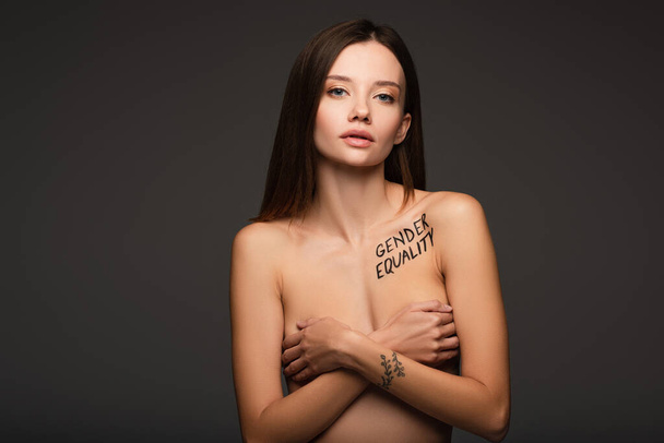 nackte Frau mit gleichberechtigtem Schriftzug auf dem Körper, die Brust unter Händen versteckt, isoliert auf dunkelgrau - Foto, Bild