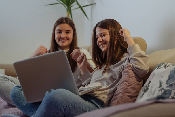 Two cheerful young girls friends sitting at the home, having fun together, using laptop - Фото, зображення
