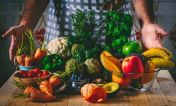 Onherkenbare man chef-kok tonen zijn seizoensgebonden verse zoete groenten en fruit producten op de tafel thuis of in het restaurant. Salade gezonde levensstijl ingrediënten voor gewichtsverlies voeding plan - Foto, afbeelding