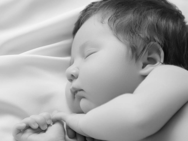 Ένα κοριτσάκι με χαμογελαστό πρόσωπο στον ύπνο. Κοριτσάκι που κοιμάται σε λευκή κουβέρτα. Όμορφο πορτραίτο μικρού κοριτσιού 14 ημερών, δύο εβδομάδων. Μητρότητα - Φωτογραφία, εικόνα