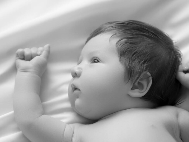 Nice newborn baby boy closeup portrait. Lying in white bed. Cute Newborn 1 month old on white sheet in diaper. Newborn care, colic, teeth, newborn day - Photo, image