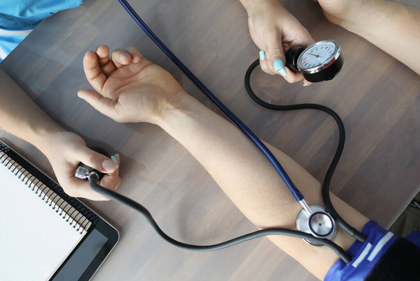 Doctor measuring blood pressure with tonometer at table in clinic closeup - Foto, Imagen