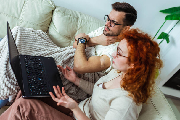 Fiatal házaspár az oltás után, akik otthoni laptoppal történő orvosi telekonzultációval. - Fotó, kép