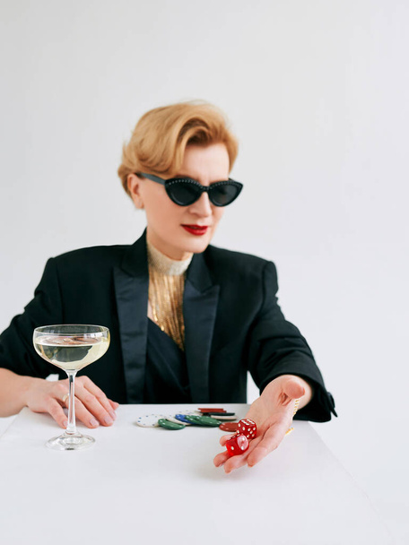 mature stylish woman in black tuxedo and sunglasses with dices in casino. Gambling, fashion, hobby concept. - Φωτογραφία, εικόνα