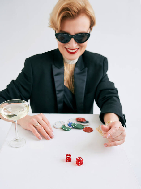 mujer con estilo maduro en esmoquin negro y gafas de sol felices de ganar en el casino. Juegos de azar, moda, concepto de hobby. - Foto, imagen
