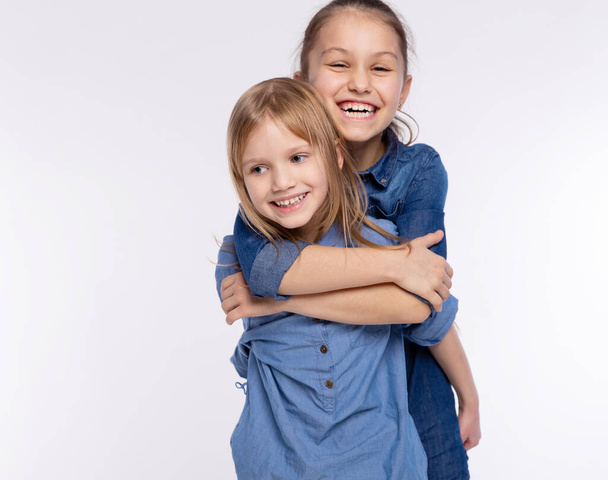 Zwei glückliche Freunde oder Schwestern, kleine Mädchen, die sich umarmen. Gemeinsam Spaß haben und emotional auf weißem Hintergrund posieren, glücklich lächelnd, Freundschaft und Beziehung Lebensstil Menschen Konzept - Foto, Bild