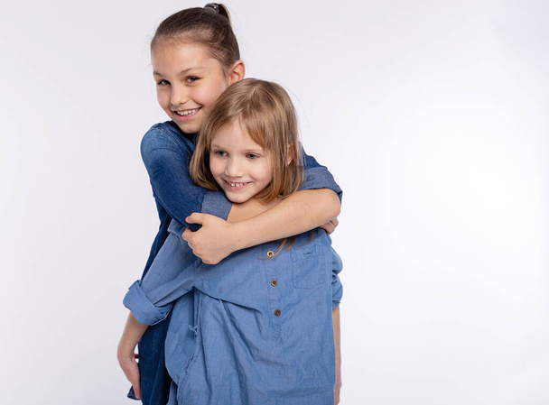 Δύο ευτυχισμένες φίλες ή αδερφές αγκαλιάζουν κορίτσια. Μαζί διασκεδάζοντας και θέτοντας συναισθηματική σε λευκό φόντο, χαρούμενο χαμόγελο, φιλία και σχέση τρόπο ζωής άνθρωποι έννοια - Φωτογραφία, εικόνα